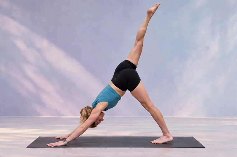 Three-legged downward dog on a yoga mat